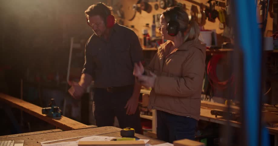 A man and woman consult a tablet while going over blueprints in a garage workshop