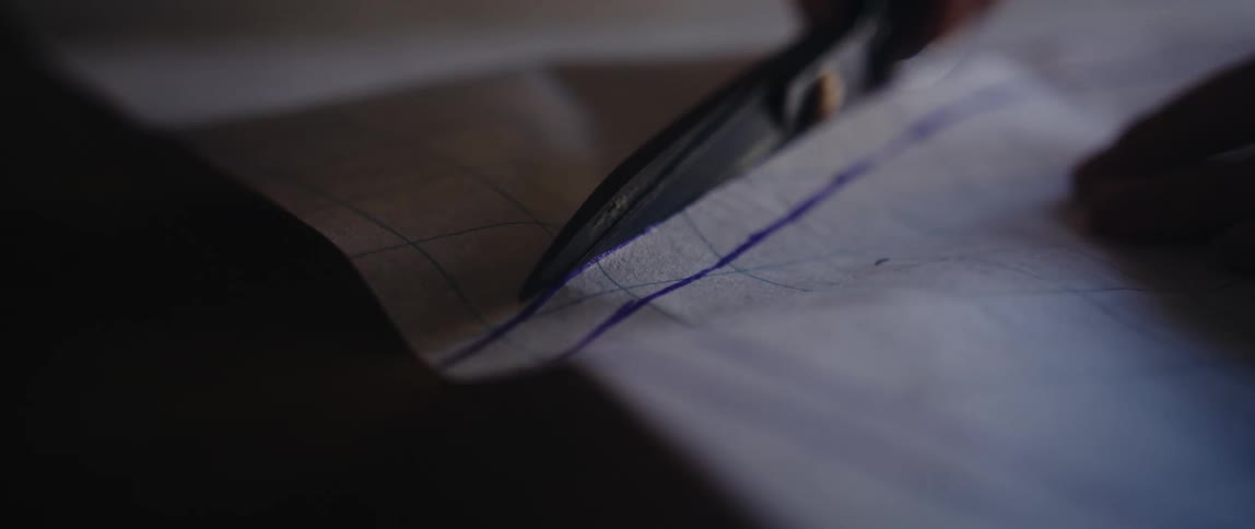 A person uses a large pair of scissors to cut off a section from a sheet of grid paper