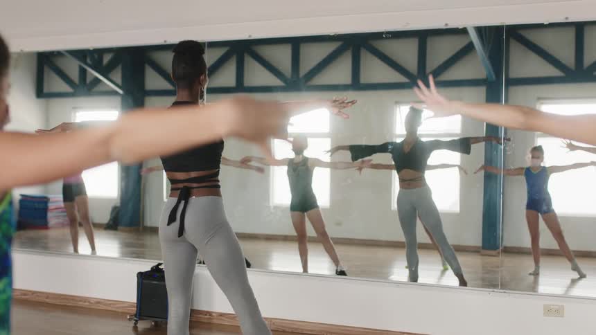 A dance instructor leads her class of teenage girls in practicing movements in a dance studio during the day