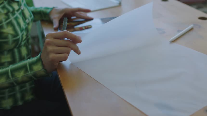 A woman sitting at a desk moves a sheet of blank paper over a tablet