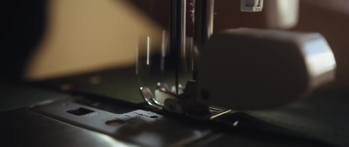 The needle of a sewing machine rapidly moves up and down as a persons hand guides the fabric