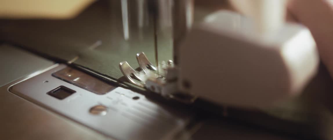 The needle of a sewing machine rapidly moves up and down as a persons hand guides the fabric