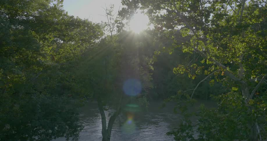 The sun rises behind a river and trees