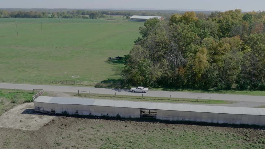 A car drives down a road past a farm