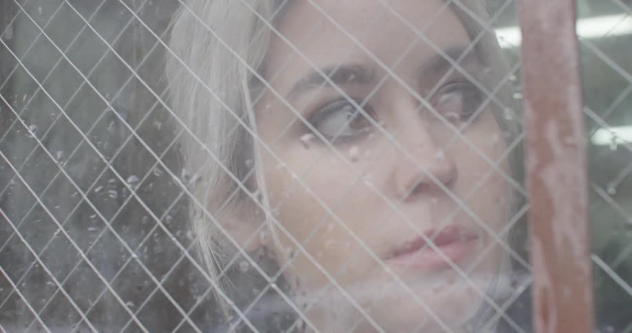 A blonde woman looks out of a wet window