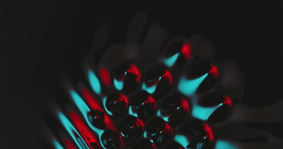 Ripples of red and blue form and flow on the surface of black liquid
