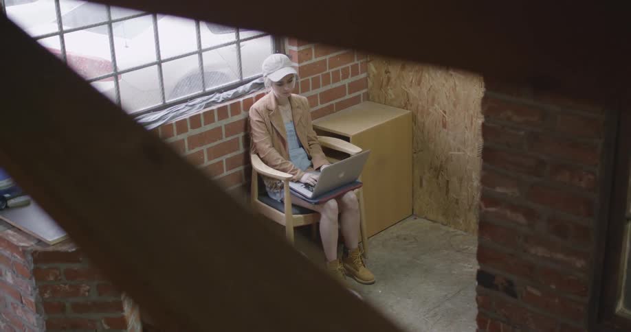A woman is sitting below by the window with a laptop