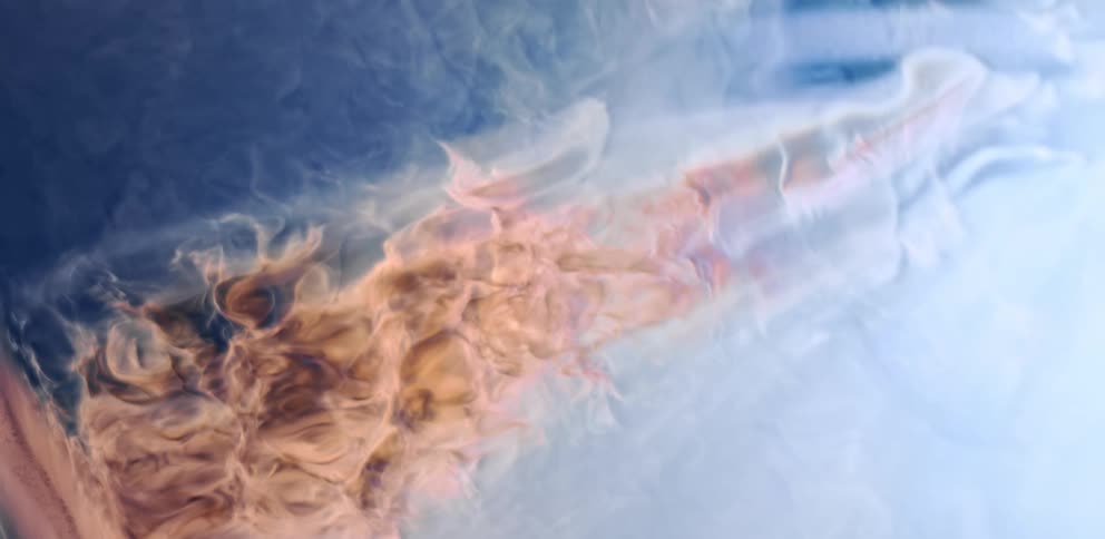 Close up of brown cream liquid ink flowing over a blue hazy background