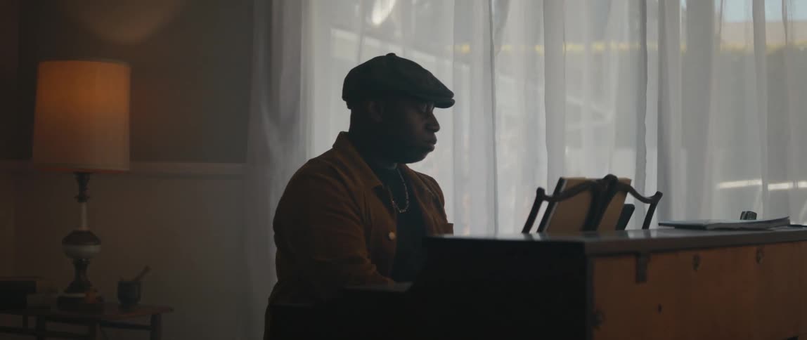 Male pianist with black cap and orange jacket plays piano in room