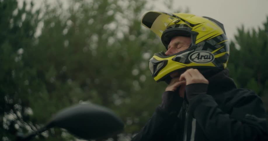 Older man puts on a crash helmet as he sits on a motorcycle