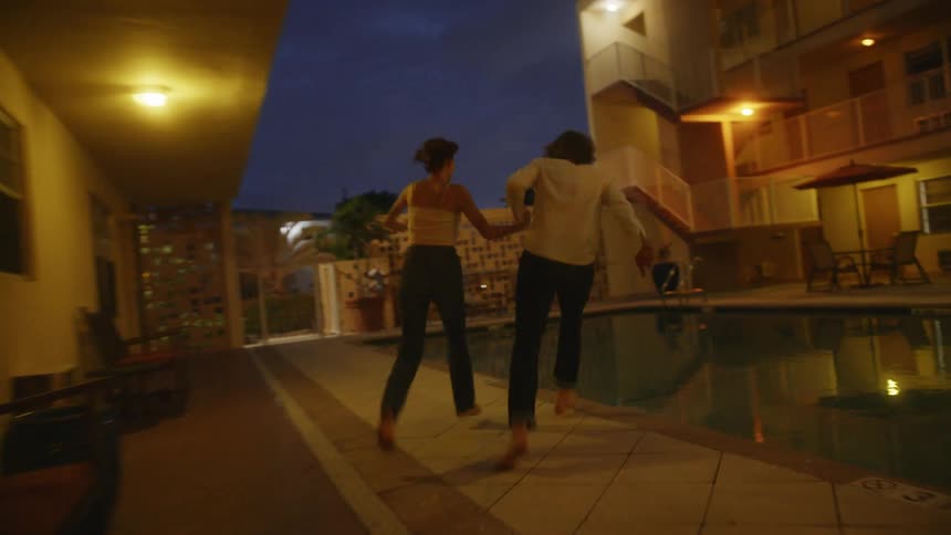 A couple is running outside and jumping into a pool