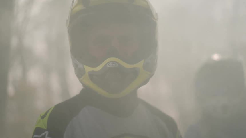 Obscuringhaze lightens enough to reveal crash helmet wearing people standing in woods