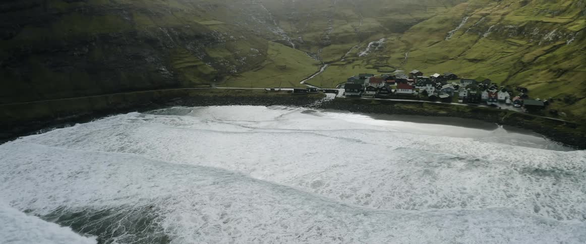 Waves crash onto shore near seaside town bordering river in valley