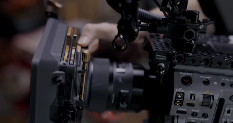 A white person is using their right thumb to adjust dials on a large video camera inside of a paneled room