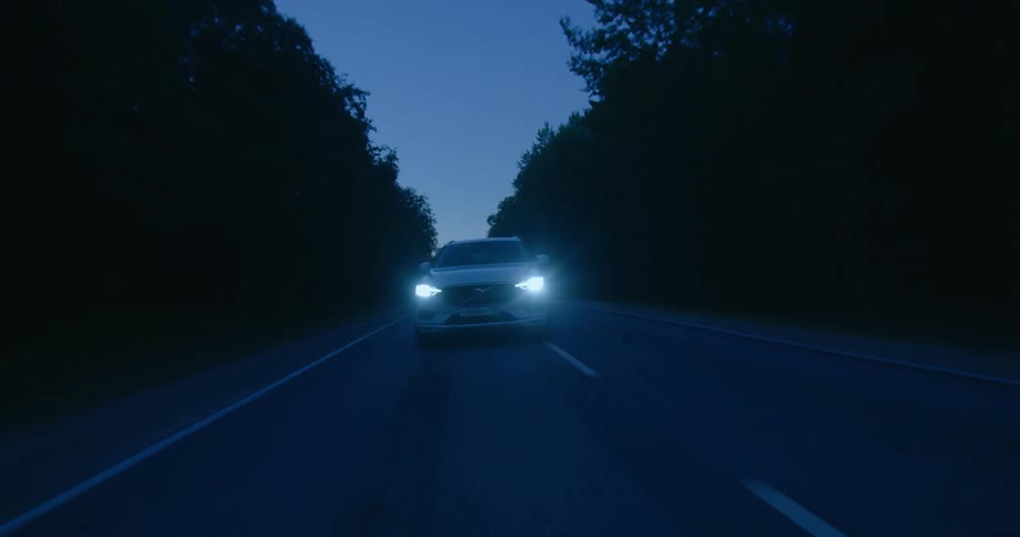 White sports car drives along highway through forest at night