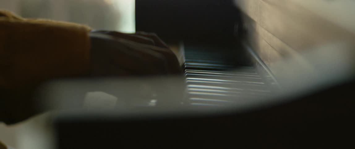 Hands of a person wearing a long yellow sleeve playing a piano during the day