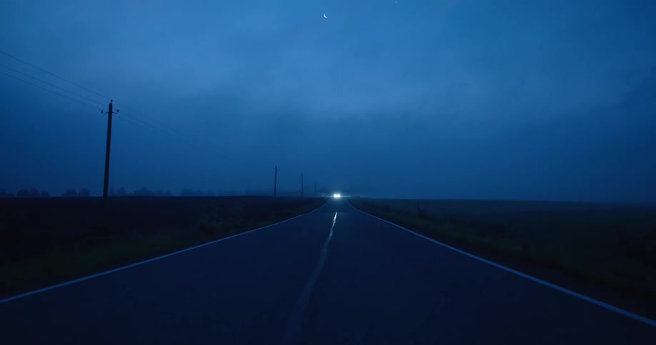 An automobile with bright headlights is in the distance on the road