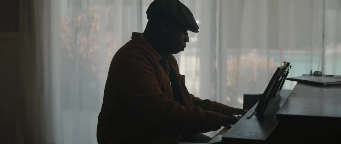 Male pianist with black cap and orange jacket plays piano in room