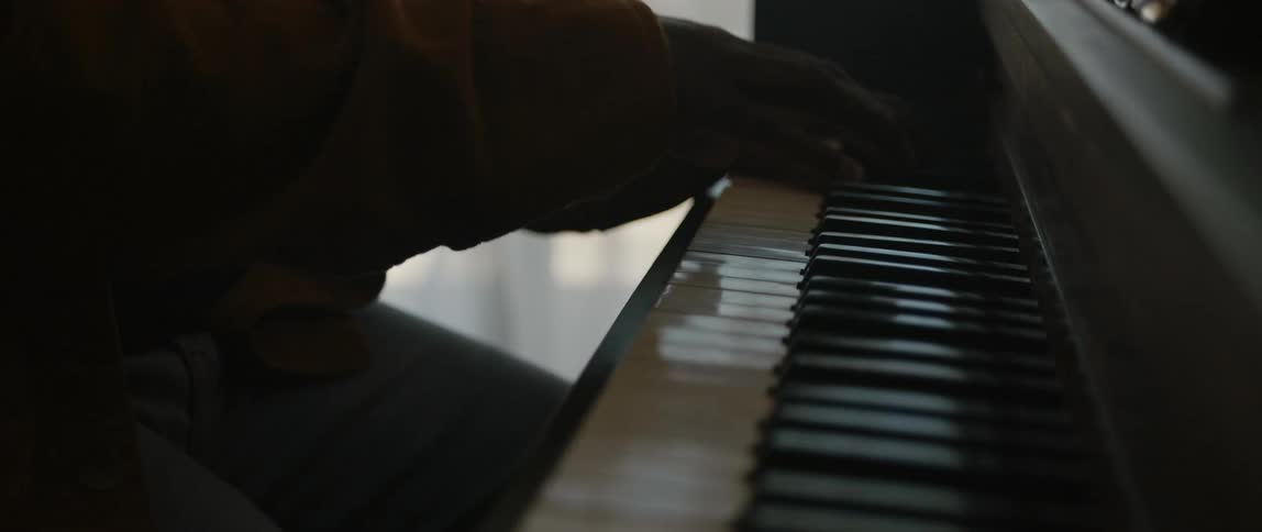 Male pianist with black cap and orange jacket plays piano in room