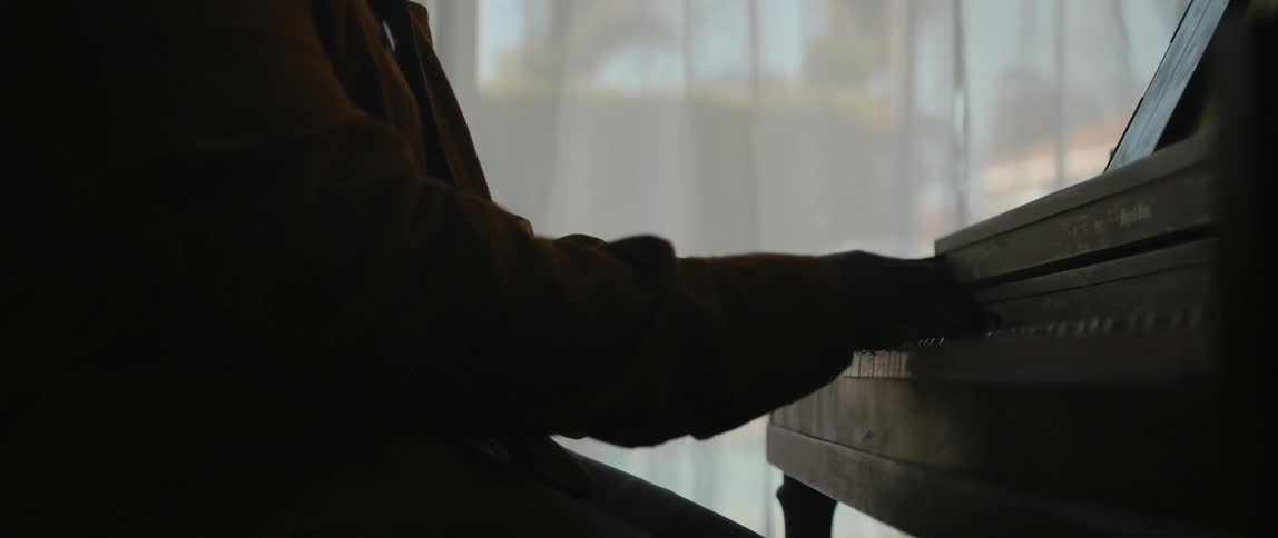 A person playing a piano in front of a curtained window