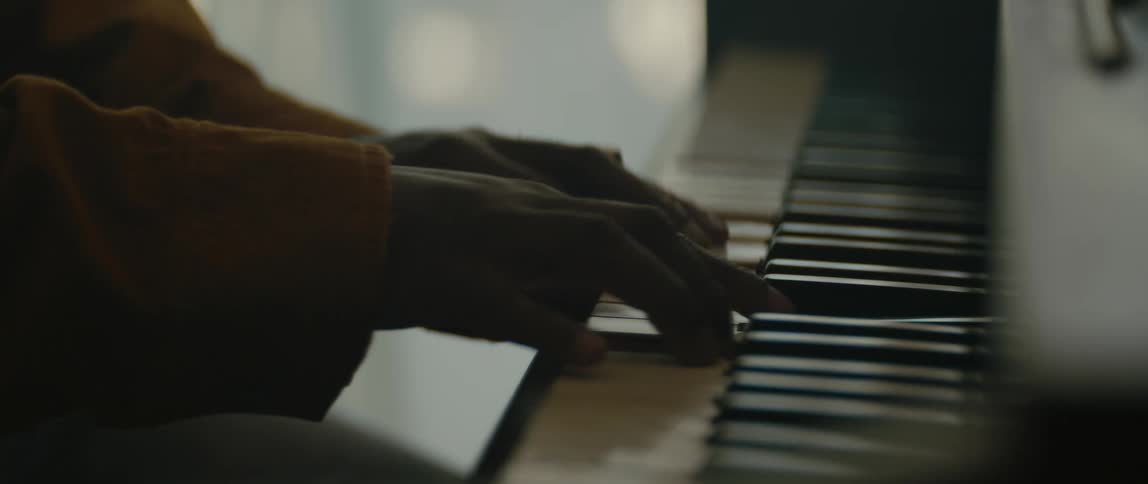 Person wearing large gold ring sits near window playing the piano