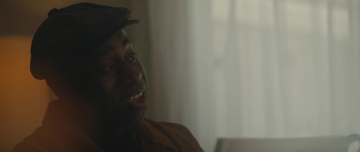 Male pianist with black cap and orange jacket plays piano and sings song in room