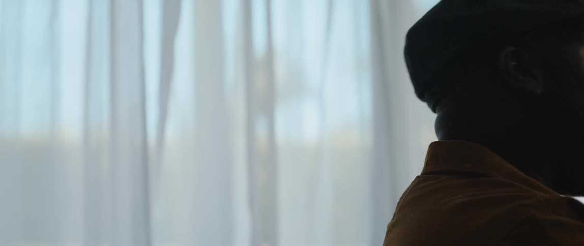 Man wearing cap sings near window with curtain