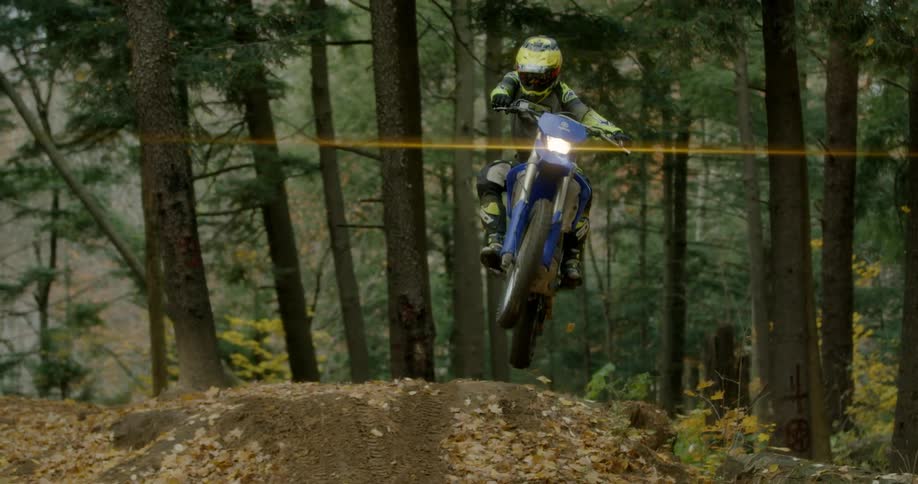 A teenager on a motorbike leaps over an embankment in the woods