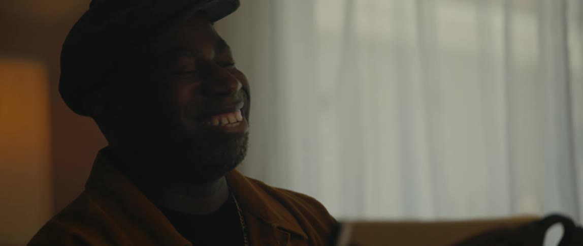 A man is smiling and sitting in a room during midday
