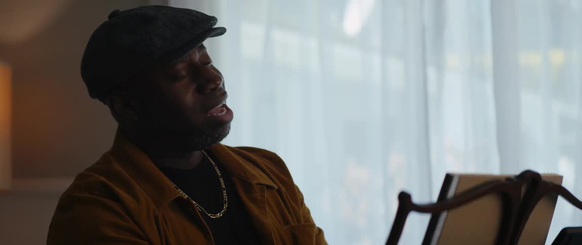 A man is sitting indoors and singing
