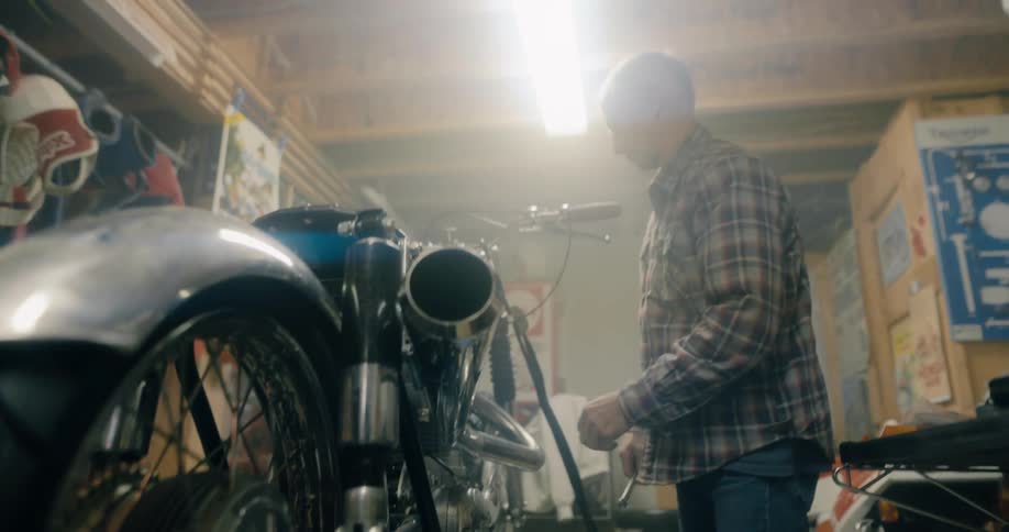 White haired man works on motorcycle in garage