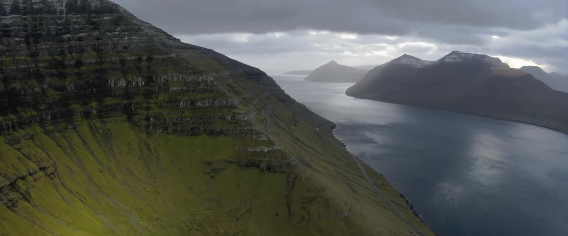 Aerial view of the green slopes of a mountain close to a great river under the clouds