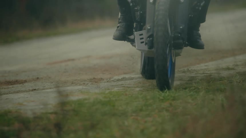 A person rides a mountain cycle off a gravel road and into the grass