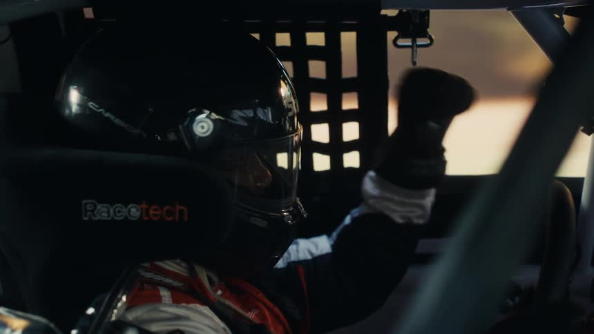 A race car driver pumping his fist in a fast moving race car