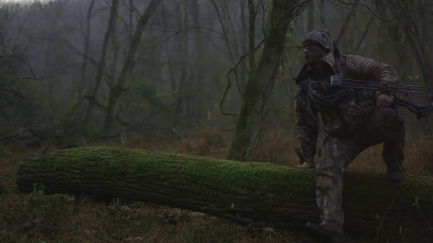 A man in camouflage gear steps over a mossy trunk
