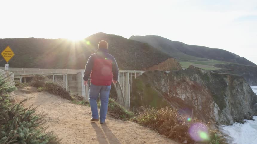 A man is hiking along a cliff leading to a bridge