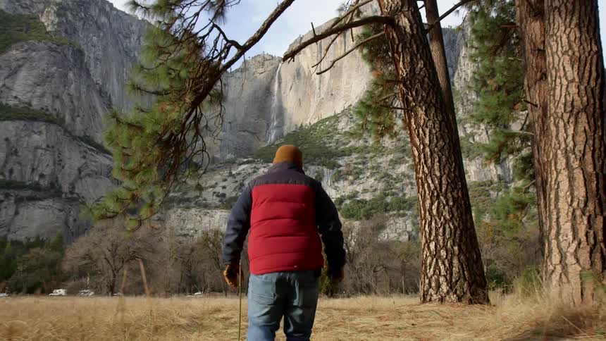 A man is walking across a long field towards a mountain