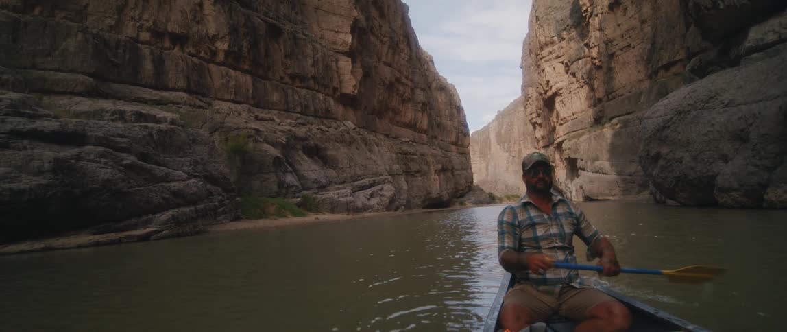 A man is rowing a canoe in a canyon river