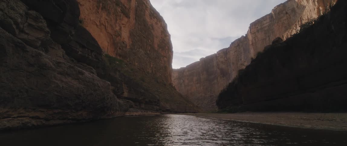There is a small piece of land along a canyon river as sunlight shines on the ripples in the water