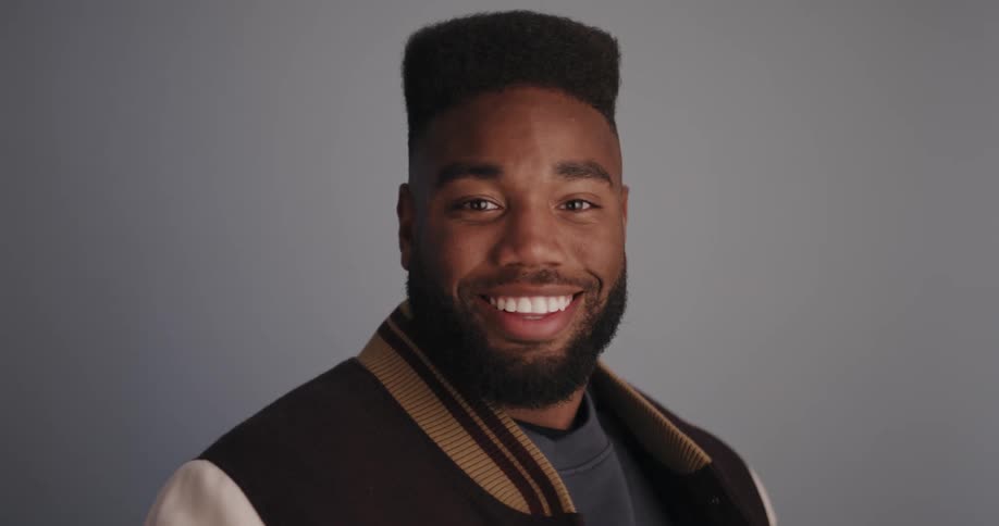 Young bearded man wearing a university jacket turns around smiling at the camera