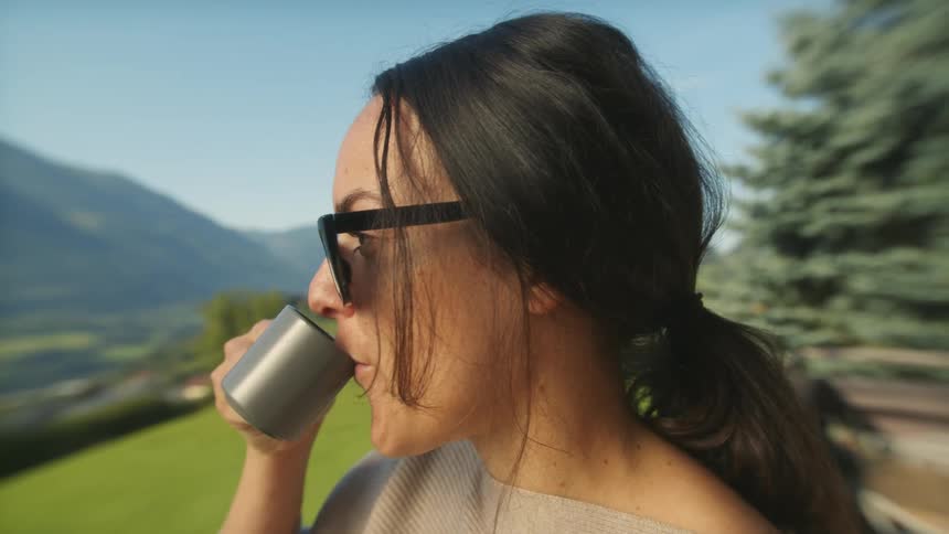 Young woman wearing sunglasses sitting outside drinking a cup of coffee on a beautiful sunny day