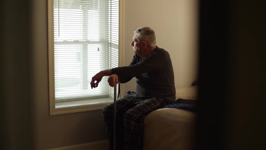 A man sits on the bed looking out the window