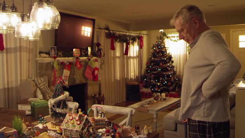 An elderly man approaching a train set in a room decorated for christmas