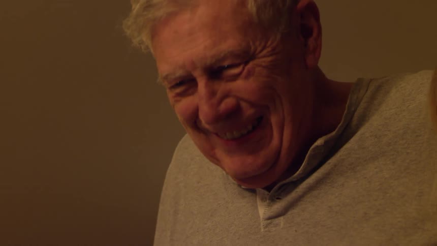An elderly man laughing and hugging a young woman