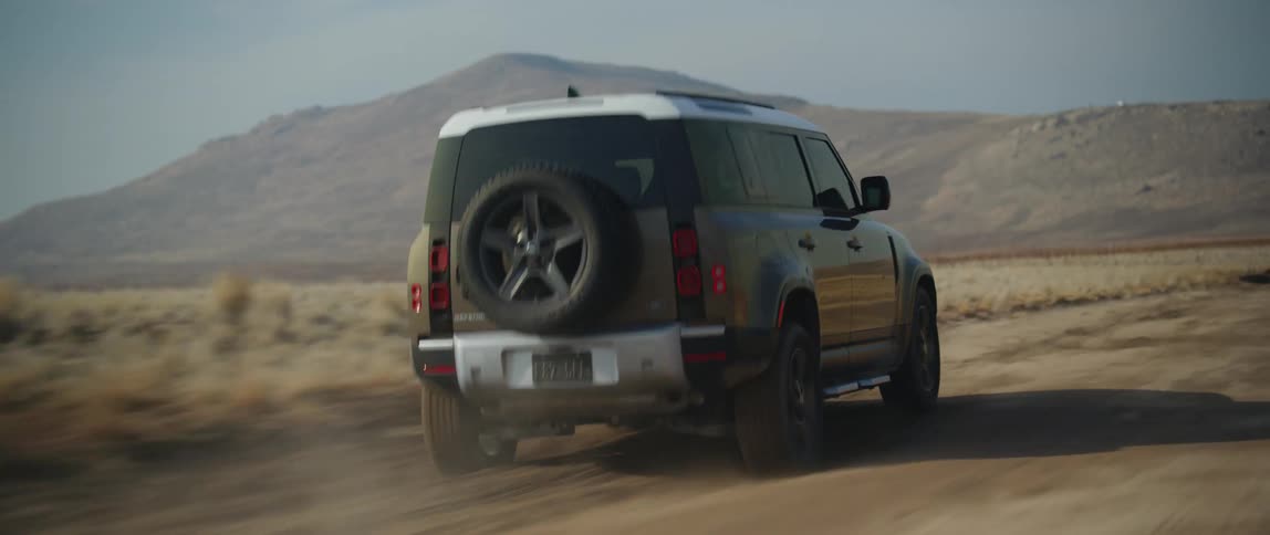 A vehicle travels along a dirt road through an arid countryside during the day