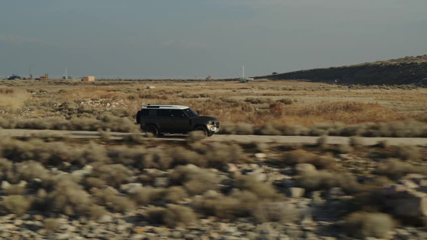 A black truck is traveling on a road across a rural desert area