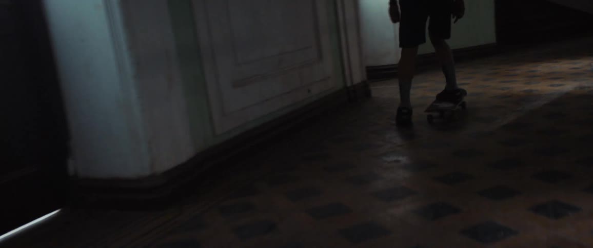 Two people are skateboarding in a hallway of a building