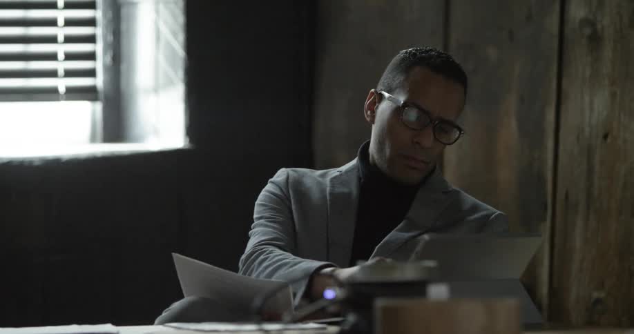 A man sits reading a paper and using a tablet