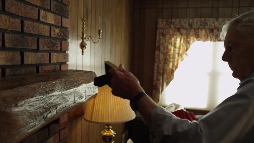 A man picks up a picture off of a mantle