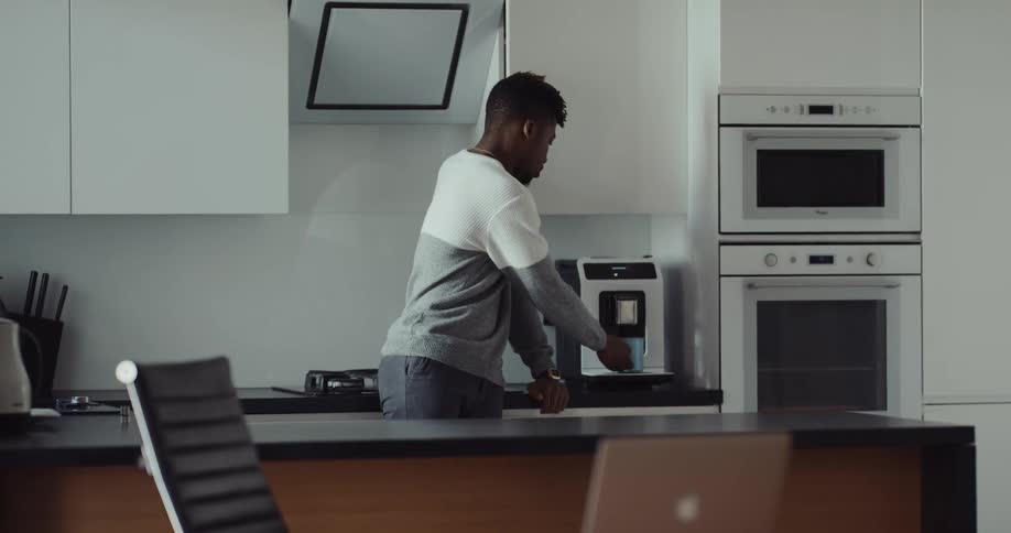 A man gets a cup of coffee from the kitchen then walks to his chair